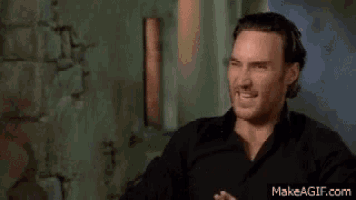a man in a black shirt is making a funny face while sitting in front of a wall .