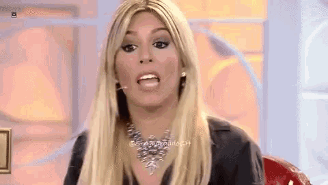 a blonde woman wearing a necklace is making a funny face while sitting on a red chair .