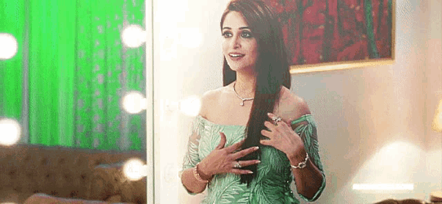 a woman in a green dress is standing in front of a mirror holding her hair .