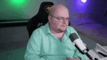 a bald man with glasses is sitting in front of a microphone in a room .