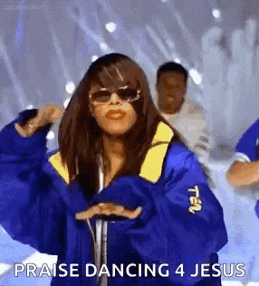 a woman in a blue jacket and sunglasses is dancing on a stage with a group of people .