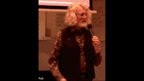 a man with a beard is holding a microphone in front of a projection screen that says fog on it