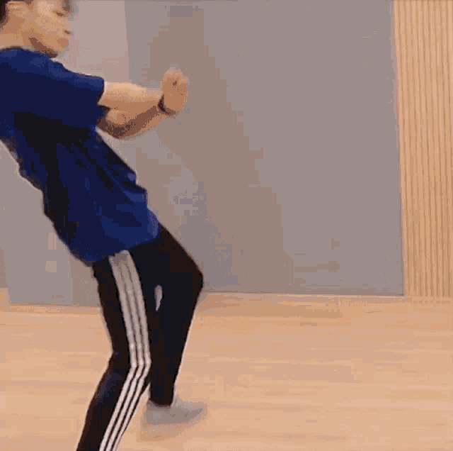 a young man in a blue shirt and black pants is dancing on a wooden floor .