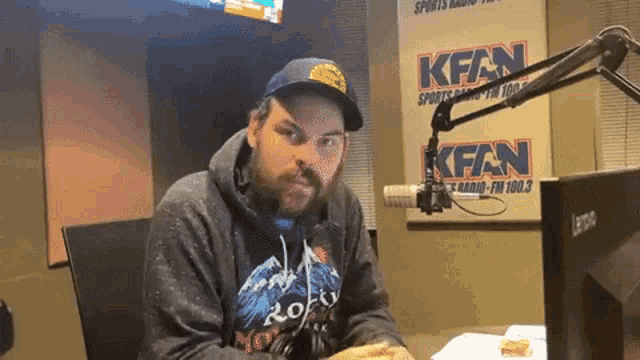a man is sitting in front of a microphone in front of a sign that says kfan on it