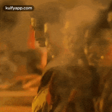 a man with a mustache is standing in front of a fire and smoking a cigarette .