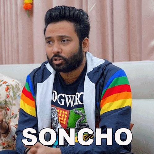 a man with a beard is sitting on a couch wearing a rainbow jacket with the word soncho on it