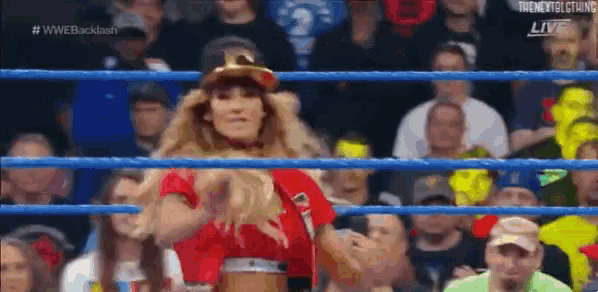 a woman in a red shirt is standing in a wrestling ring with a crowd watching .