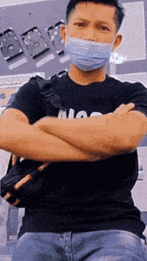 a man wearing a mask and a black shirt is sitting with his arms crossed .