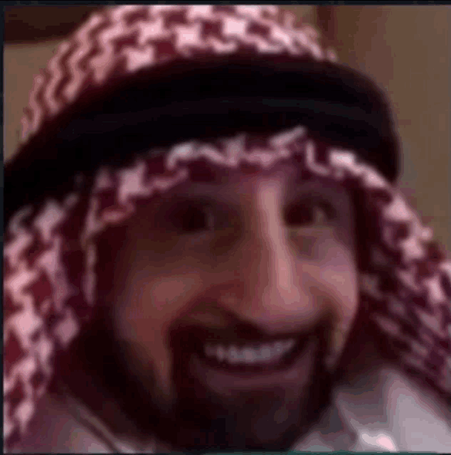 a man with a beard is wearing a head scarf and a hat .