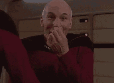 a man in a red sweater is covering his mouth with his hands while laughing .