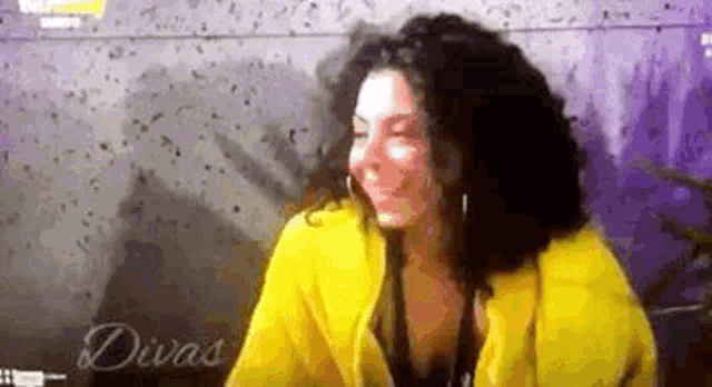 a woman with curly hair wearing a yellow jacket is smiling .