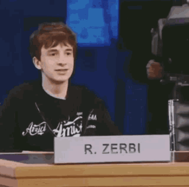 a young man is sitting at a table with a sign that says r. zerbi