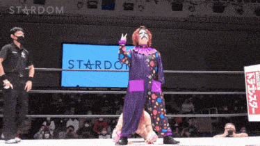 a wrestler in a clown costume stands in front of a stardom screen