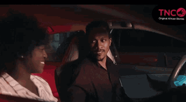 a man and a woman are sitting in a car with a tnc logo in the corner
