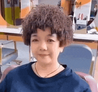 a woman with a wig on her head is sitting in a chair at a hair salon .