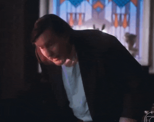 a man in a suit is standing in front of a stained glass window in a dark room .