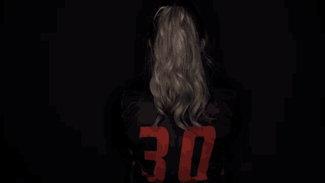 a woman wearing a campbell jersey stands in the dark with her arms crossed