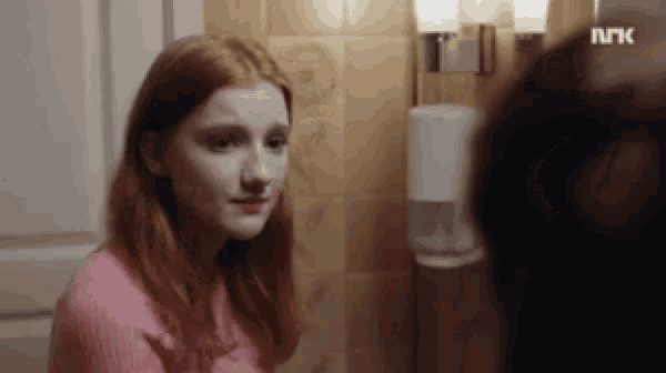 a woman in a pink sweater is looking at herself in the mirror .