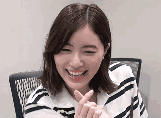 a woman in a striped shirt is smiling and making a peace sign