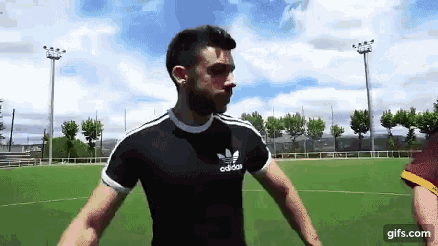 a man wearing an adidas shirt is standing on a field