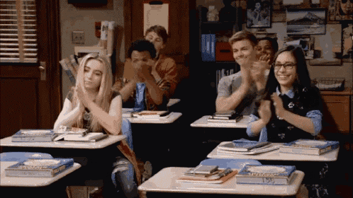 a group of students are clapping in a classroom while sitting at desks