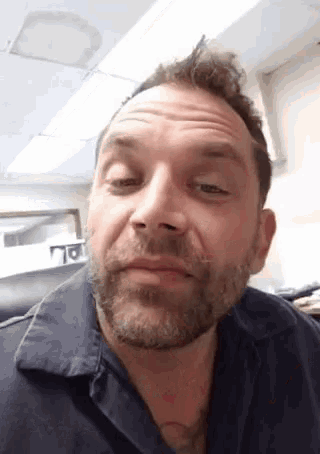 a man with a beard and a blue shirt is making a funny face