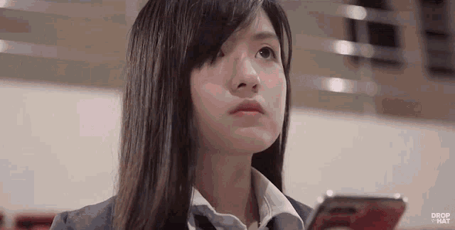 a girl in a school uniform is holding a cell phone in her hand .