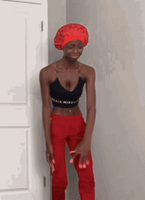 a woman wearing a black nike crop top and red pants is standing in front of a door