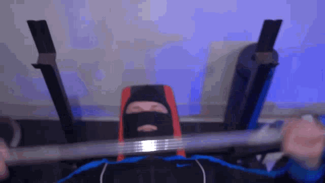 a man wearing a black mask is lifting a barbell on a bench