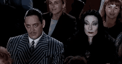 a man in a suit and tie is sitting in a crowd with a woman in a black dress .