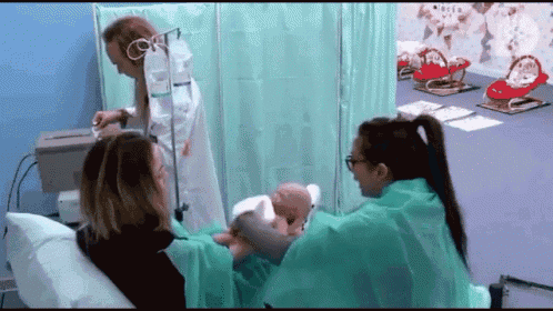 a woman is sitting in a hospital bed with a baby while a doctor looks on .