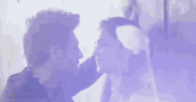 a man and a woman are looking at each other in a purple light .