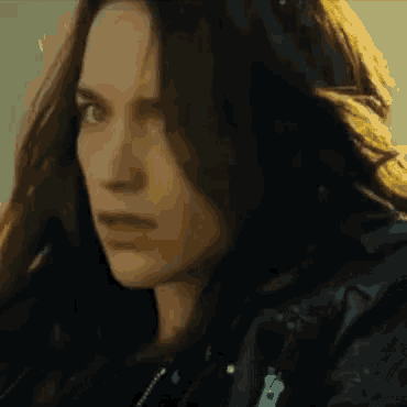 a woman with long dark hair is wearing a black leather jacket and looking at the camera .