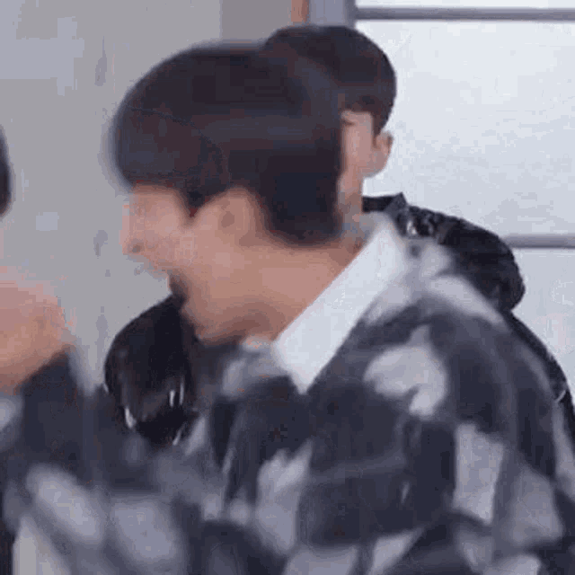 a man in a plaid sweater is laughing while standing next to another man in a room .