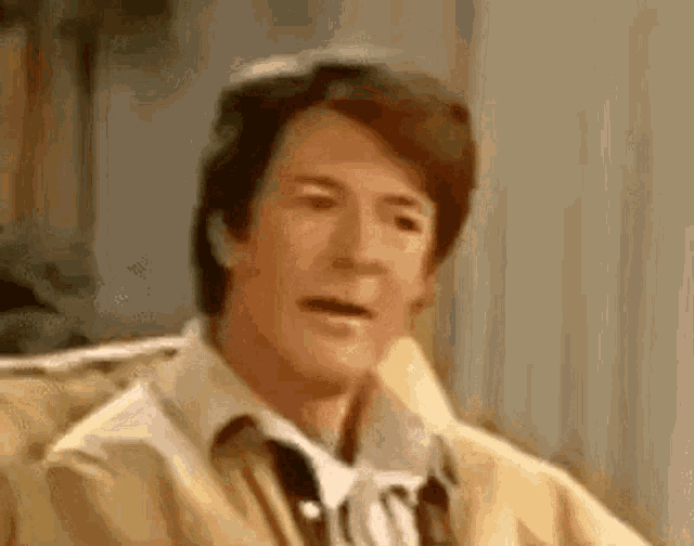 a man in a yellow jacket is sitting on a couch and making a funny face .