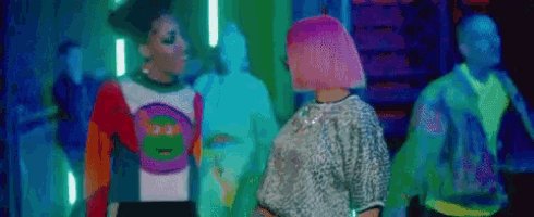 a woman with pink hair is standing next to another woman in a colorful outfit .