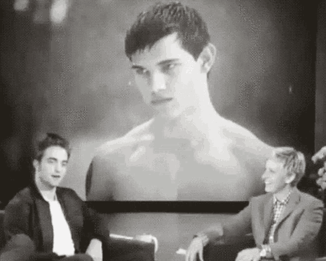 two men are sitting in front of a screen with a picture of a shirtless man .