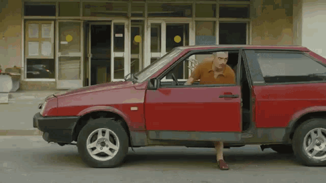a man is getting out of a red car with the door open