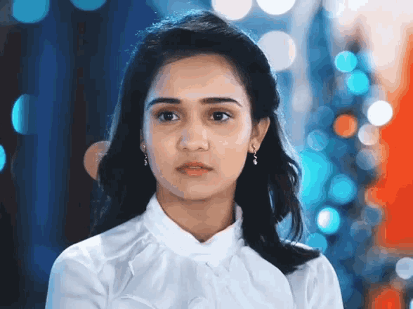 a woman wearing a white shirt and earrings looks serious