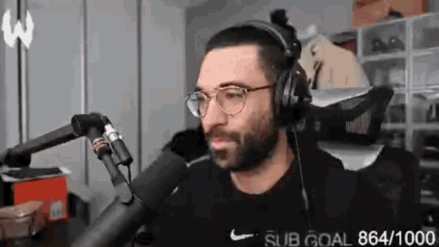 a man with a beard is wearing headphones and glasses while talking into a microphone .