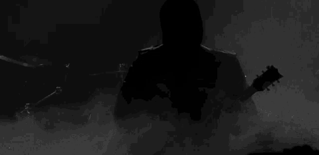 a man in a hood is playing a guitar in the dark