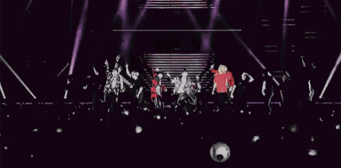a group of people are standing on a stage in front of a crowd of people holding balloons .