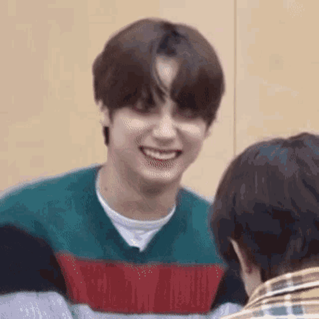 a young man in a striped sweater is smiling while sitting next to another man .