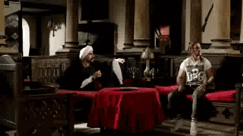 two men are sitting at a table in a room with columns .
