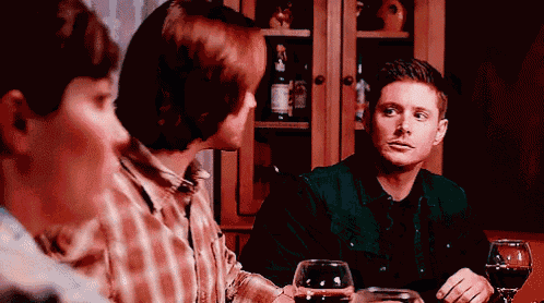 a group of men are sitting at a table with wine glasses and talking .