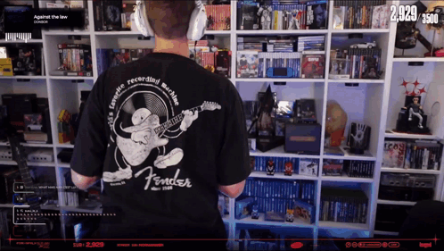 a man wearing a black fender t-shirt stands in front of a shelf full of dvds