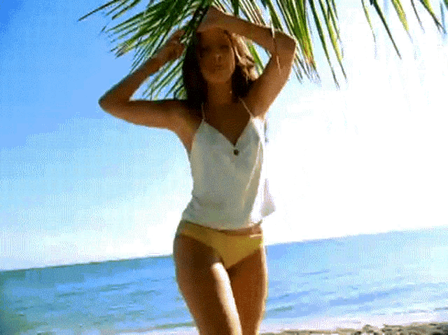 a woman in a white tank top and yellow bikini stands on the beach