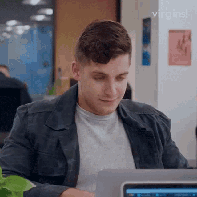 a man is sitting in front of a laptop computer with the words virgins written above him .