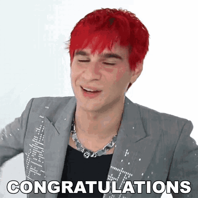 a man with red hair is wearing a grey jacket and a necklace and says congratulations