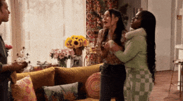 three women standing in a living room with a yellow couch